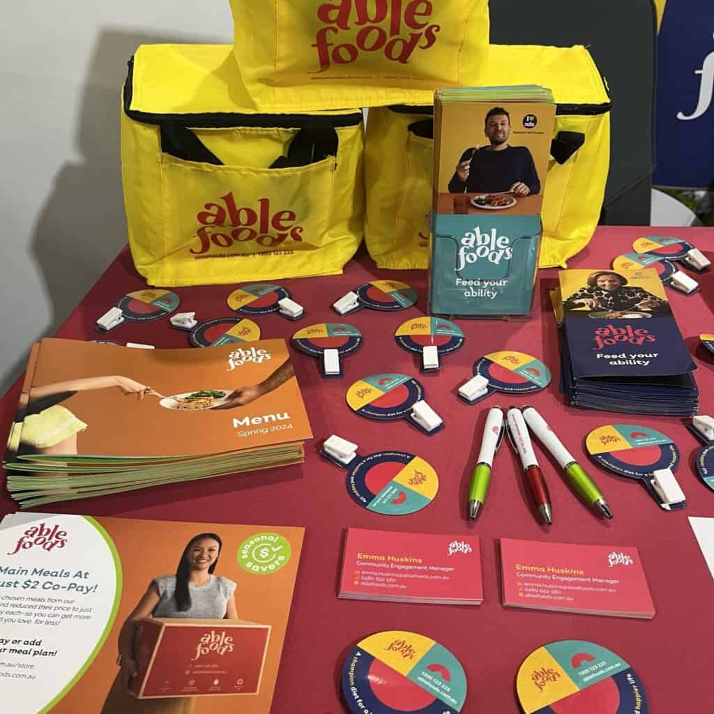 A table of free items including colourful magnets, pens, and cooler bags for our meals. It also has menus, brochures, and flyers.