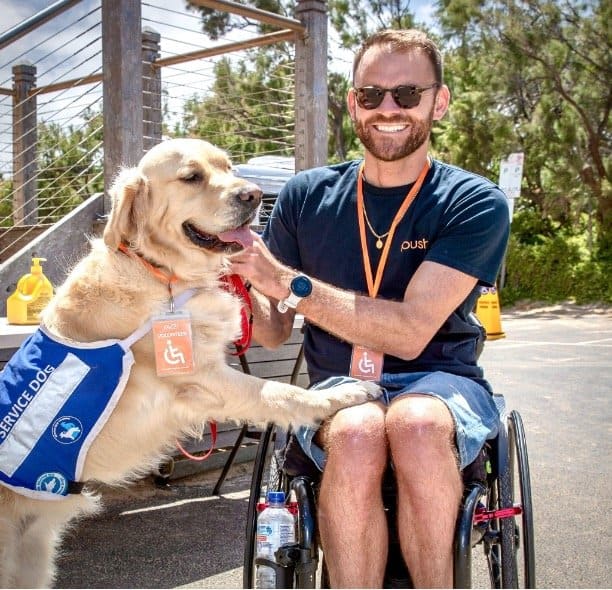 Shane Hryhorec in a wheelchair at the beach with a golden retriever