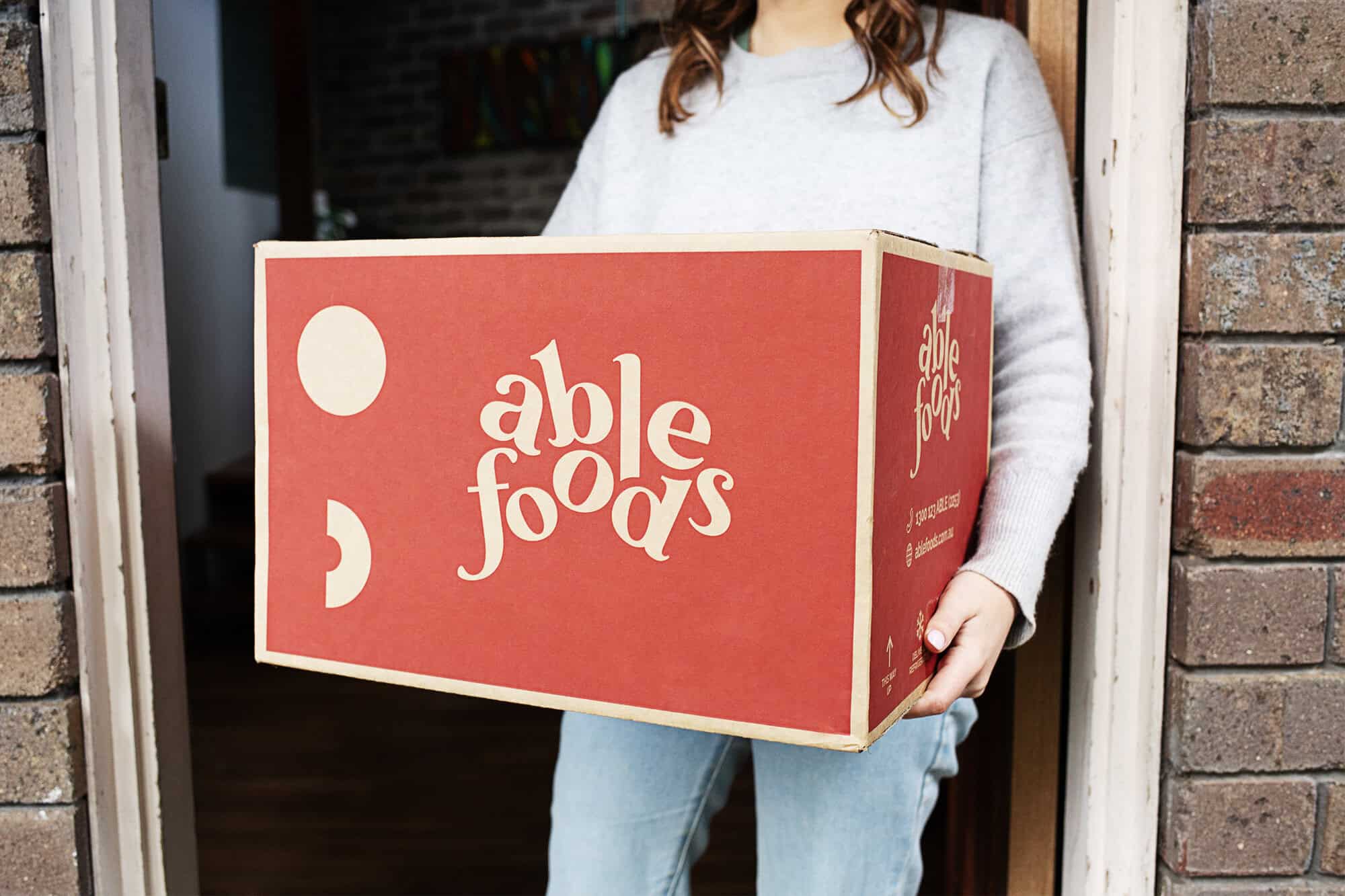 Woman holding an Able Foods box at her front door