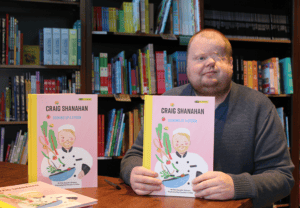 Craig Shanahan holding up his new book, cooking up a storm